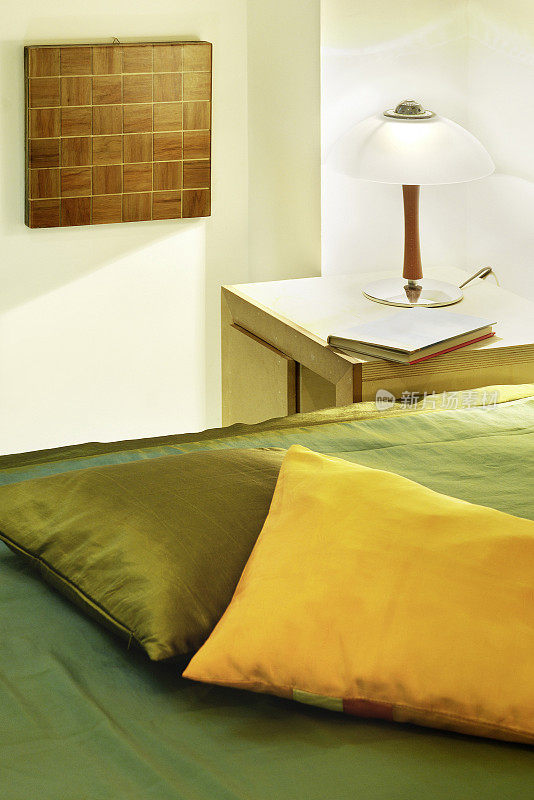 卧室的细节:枕头，灯，床头柜，书，木墙艺术品