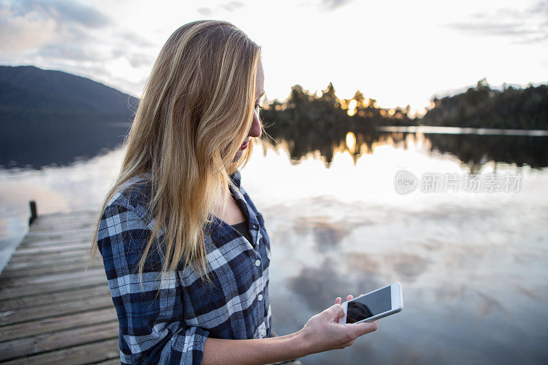 金发女孩站在湖边码头上发短信
