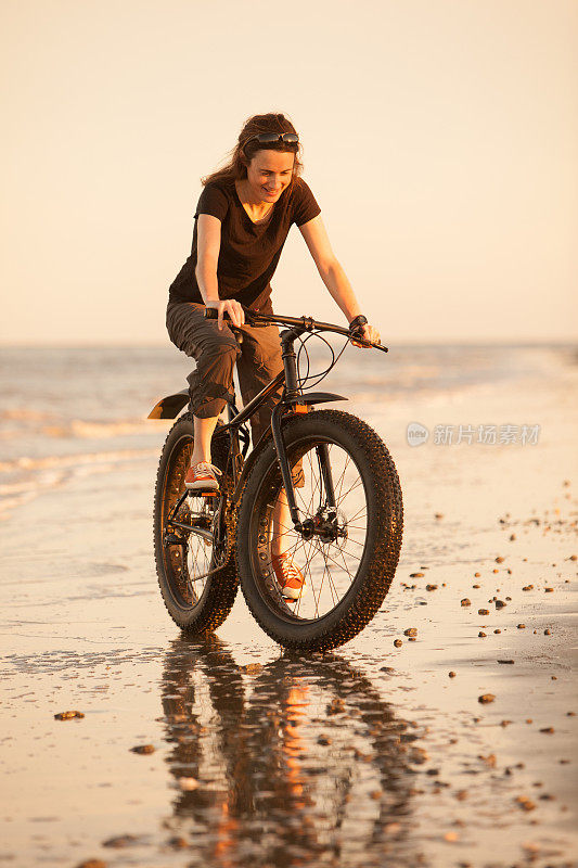 有魅力的女人在海滩上骑着她的胖自行车。