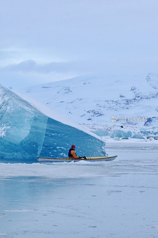 一名男子在冰岛巨大的冰山周围划桨。