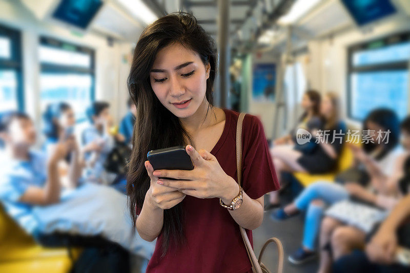亚洲女性乘客与休闲服装通过智能手机使用社交网络在BTS轻轨或捷运地铁在大城市旅行，生活方式和交通理念