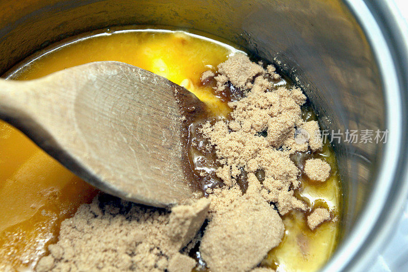 用木勺在铁架上的平底锅里搅拌红糖和融化的黄油