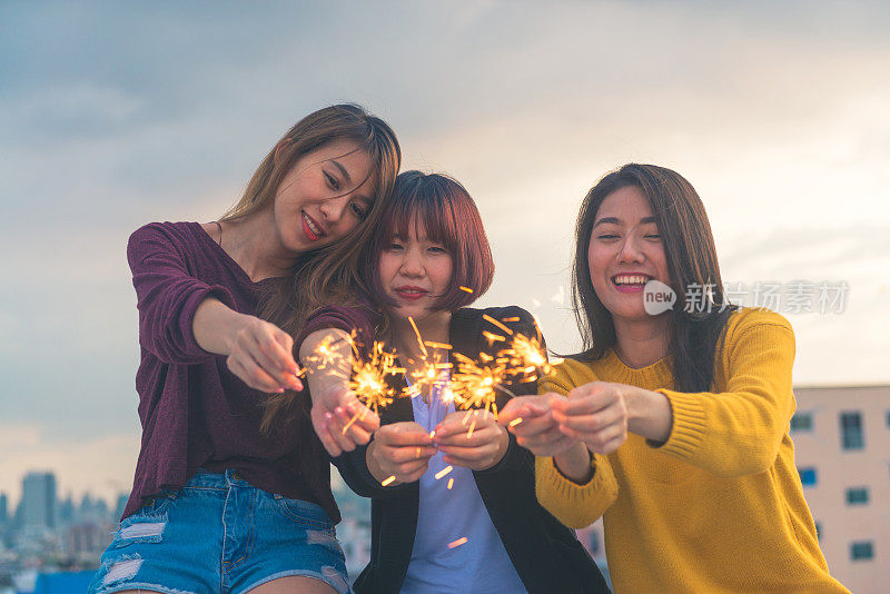 户外拍摄的年轻人在屋顶派对。快乐的一群亚洲女孩朋友享受和发挥火花在屋顶派对傍晚日落。节日庆祝节日派对。青少年的生活方式。