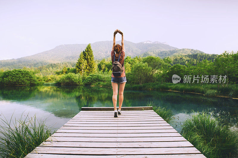 一名年轻女子站在木桥上，双手高举，背景是大自然。