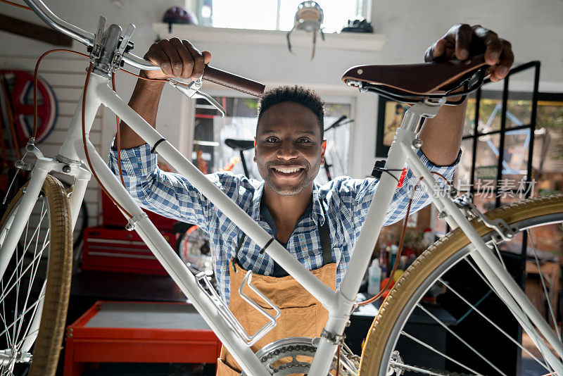 一个快乐的黑人企业主在他的自行车车间看着照相机微笑的肖像