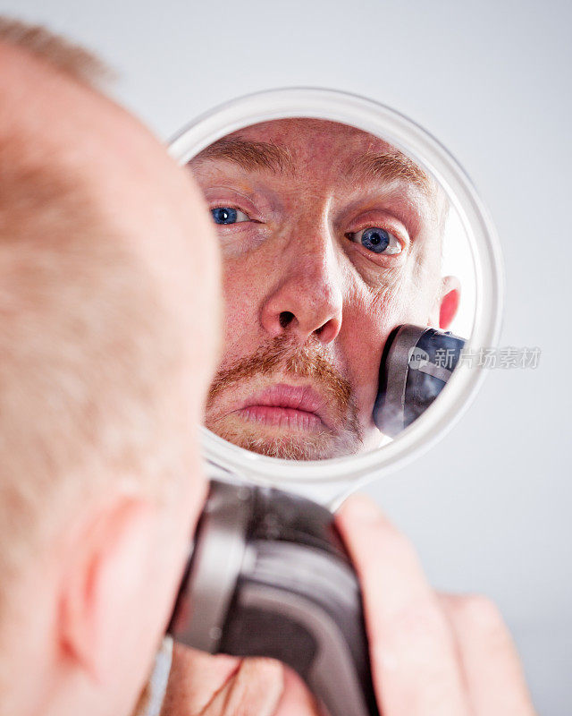 男人在镜子里看着自己刮起的山羊胡
