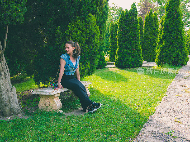 女孩坐在美丽的花园里的长椅上