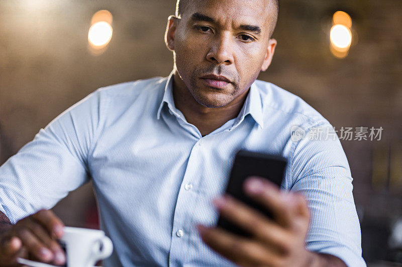严肃的非裔美国商人在咖啡馆用手机。