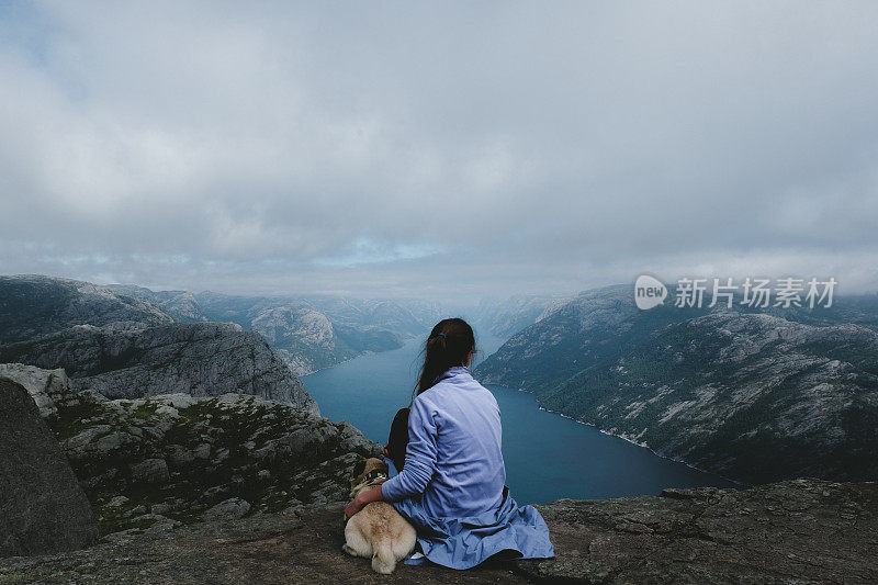 一个女人和一只狗在看挪威布道石上吕瑟峡湾的风景