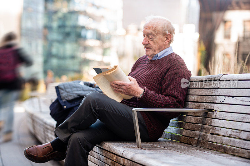 高级男子坐在户外阅读在美国纽约的高架线上