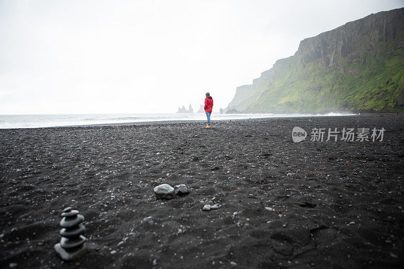 一个年轻人站在冰岛的黑沙滩上凝视着大海