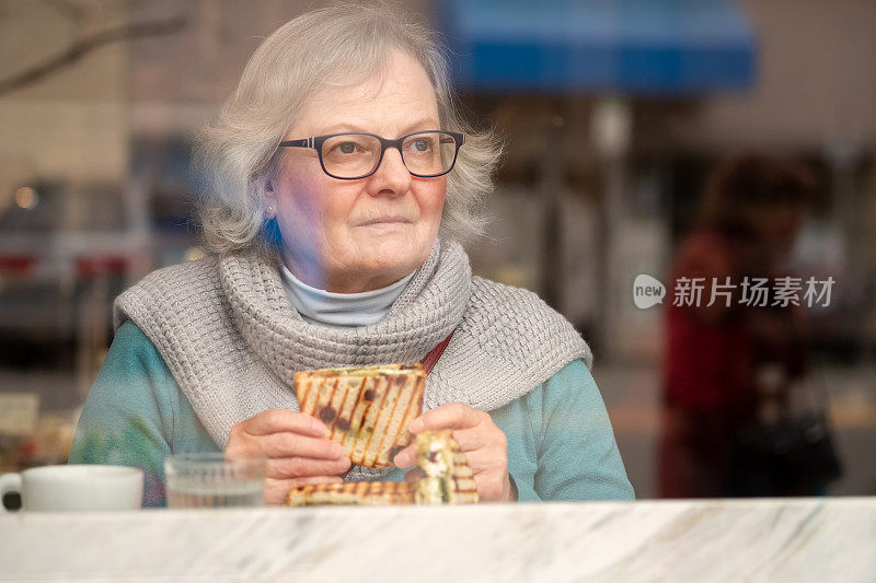 老妇人一边吃素食三明治一边看窗外