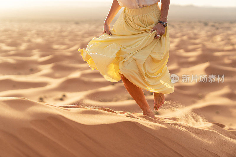 梅尔祖加(撒哈拉)沙漠的日出。一个年轻的白种女人跑过沙丘的顶部，用她的手拿着黄色的长裙。
