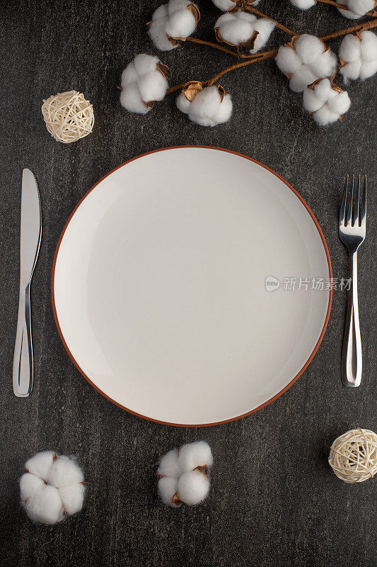 用刀叉清空白色盘子，在石板背景上放上棉花树枝，为你的菜单或食谱留出复制空间。菜单卡餐厅和餐桌设置。垂直的照片。平躺