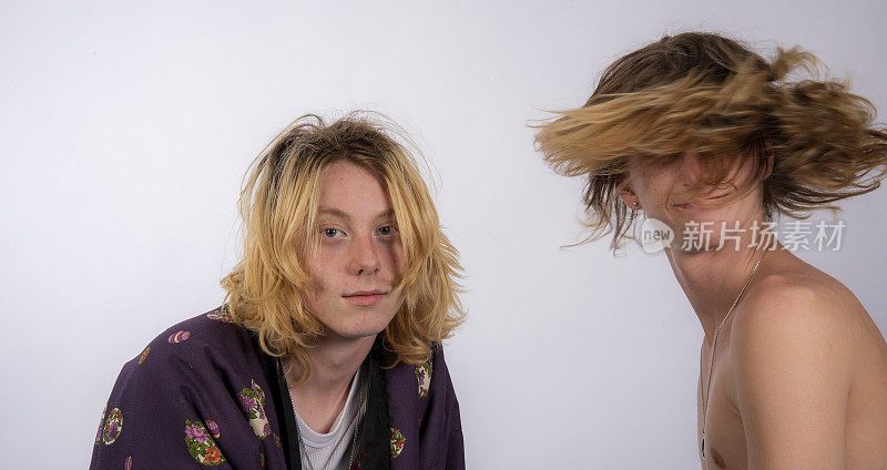 年轻的男音乐家随着音乐的节拍甩动头发，而他的朋友却在看镜头。