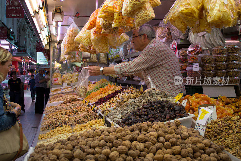 老男性市场小贩从他的市场摊位上拿出一袋食品，主要是坚果、无花果和干果