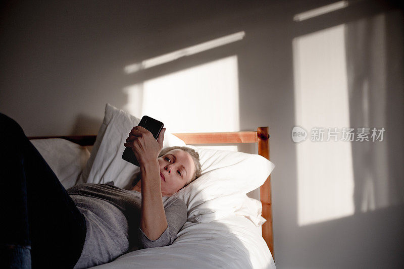 成熟的女人在床上拿着手机