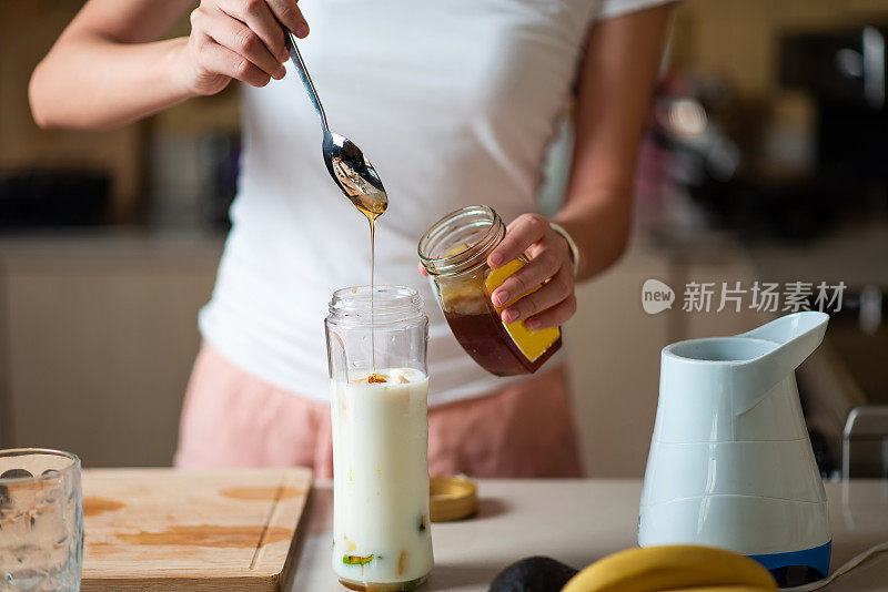 一名女子在制作牛油果香蕉奶昔时加入蜂蜜，作为健康的早餐饮料