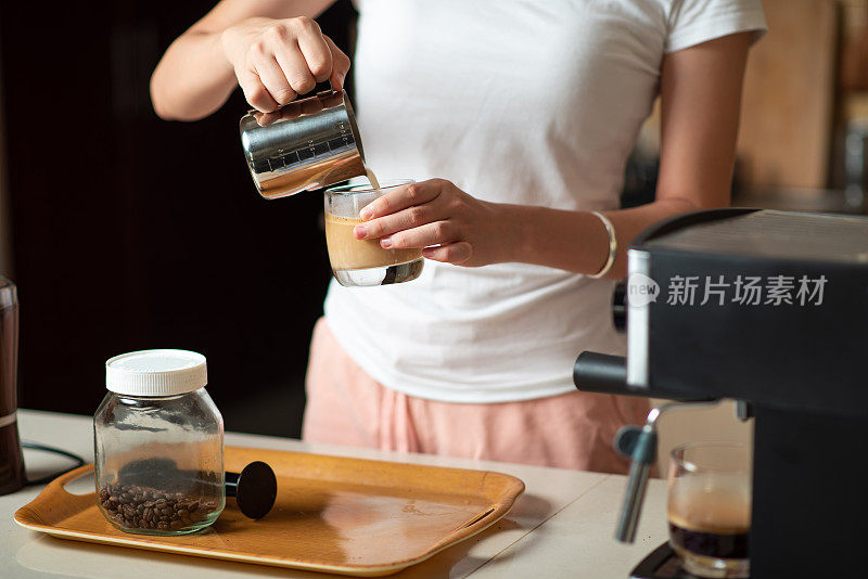 一名女子在制作拿铁卡布奇诺咖啡时，将牛奶泡沫倒进意式浓缩咖啡