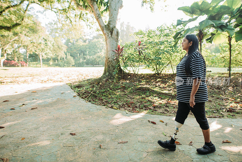 在阳光明媚的日子里，亚裔印度残疾人微笑着在公园里散步和锻炼