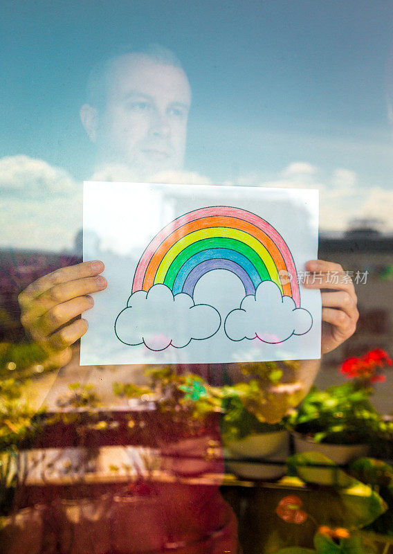 2019冠状病毒病大流行期间，一名男子在窗口举着彩虹