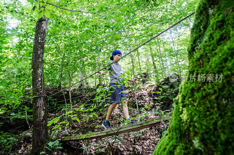 男孩走在森林里的吊桥上