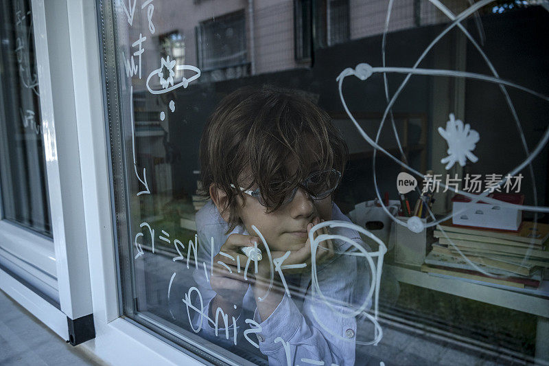 天才男孩在窗户上写公式。