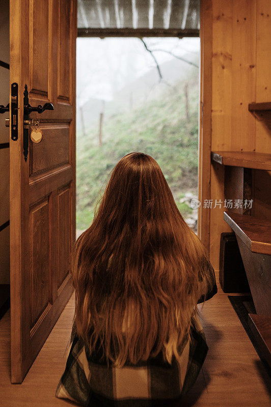 后视图的年轻女子坐在一所房子的入口处
