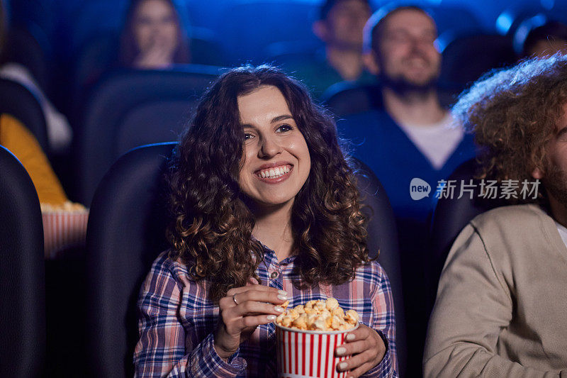 年轻的笑女孩在电影院吃爆米花。