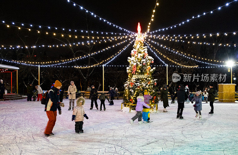 一个美丽的冰场全景装饰着圣诞树和照明与儿童和成人。运动模糊