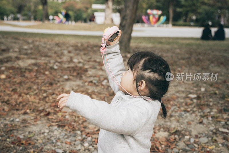 一个亚洲小女孩在公园里玩玩具相机