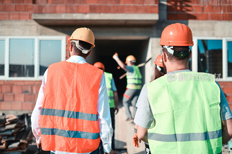 建筑师和土木工程师跟随工人进入建筑工地的后视图