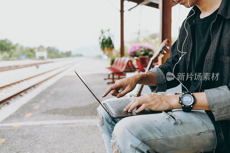 年轻的亚洲人使用笔记本电脑工作和搜索位置的旅行在火车站。自由职业者工作和旅行的概念。