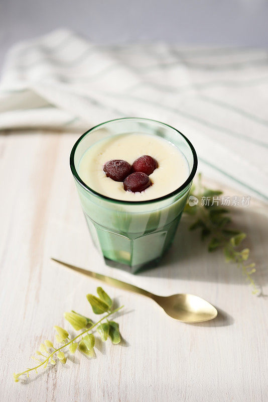 白木背景的绿杯米布丁，用冷冻樱桃装饰