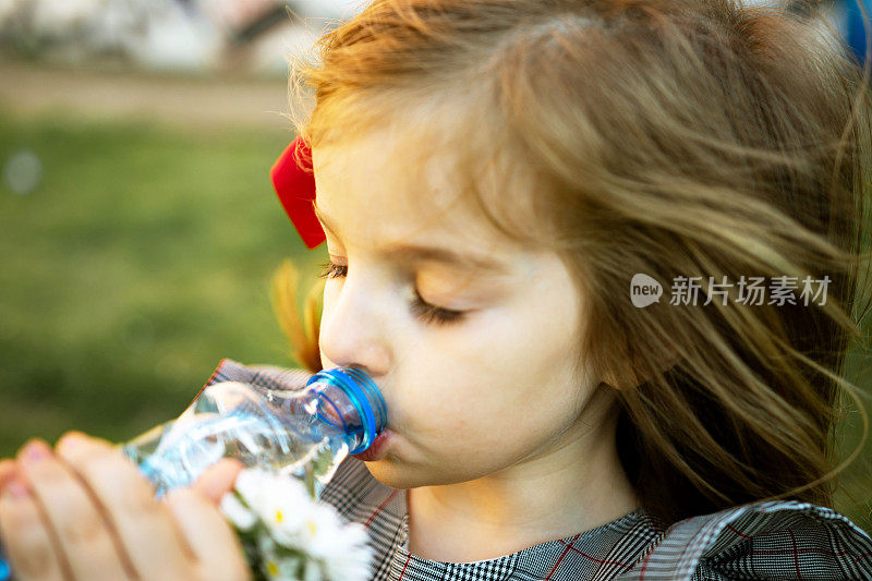 美丽的小女孩正在喝瓶子里的干净水。炎热的夏天