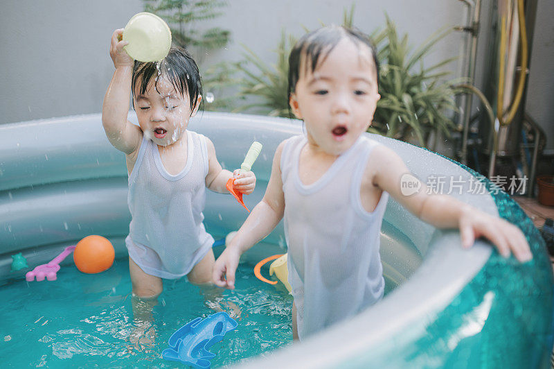 炎炎夏日，一对亚洲华人双胞胎男婴在自家后院的充气游泳池里玩耍