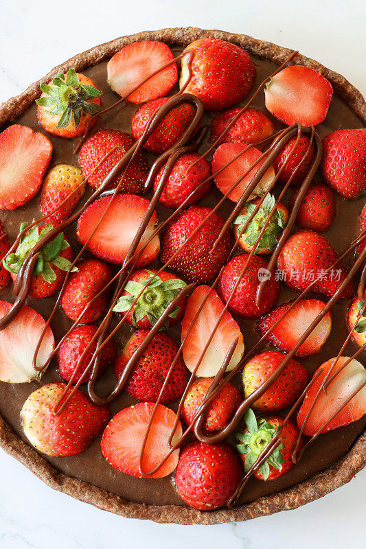巧克力草莓挞的特写图像，酥脆的，有凹槽的可可酥皮，上面覆盖着整个和减半的草莓，淋着融化的巧克力，大理石效果的背景，升高的视野