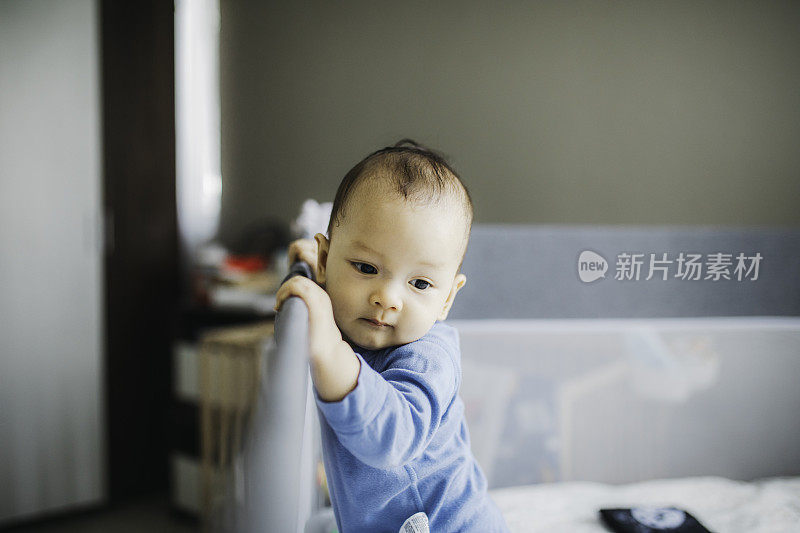 人像亚洲宝宝站着，抱着床架