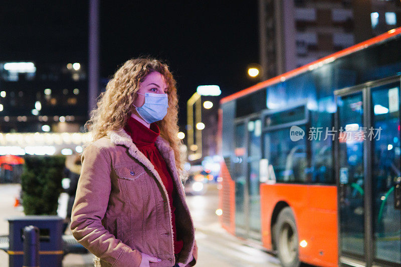 一个戴着口罩在晚上等公交车的女人