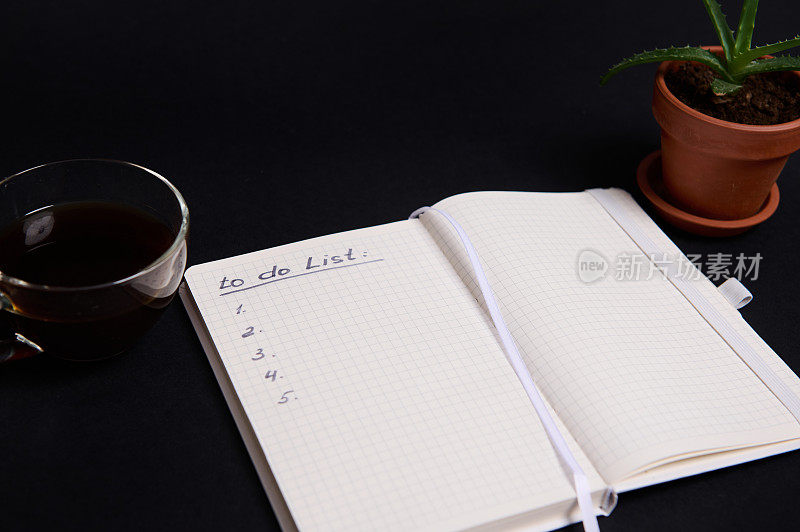 打开的记事本，白纸上写有待办事项清单的记事本，一杯咖啡和一壶多汁的陶罐，黑色背景上有复制空间。商业，组织，时间管理的概念。