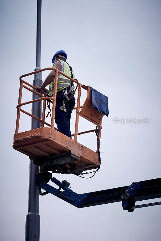 手工工人在伸缩吊篮上固定街灯杆。