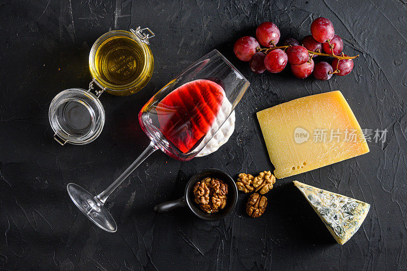 葡萄，红酒，奶酪，蜂蜜和坚果，梅洛红酒，玻璃开胃菜。黑石桌俯视图