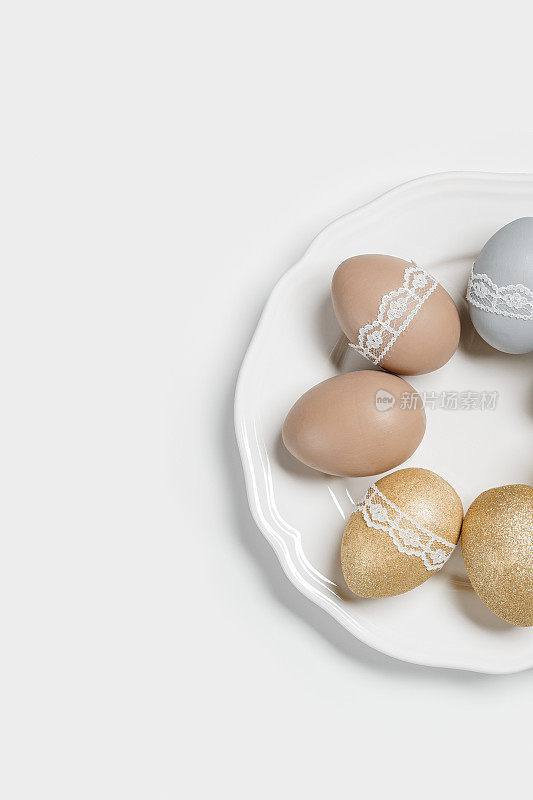 染色复活节蛋彩色粉笔金色，灰色，米色在白色的盘子。复活节节日快乐，庆祝美食理念，鸡蛋中性新潮色彩和蕾丝带装饰。顶视图表