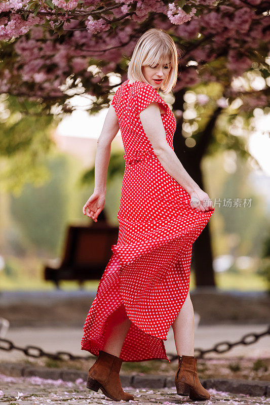 在春天的城市里穿着红色裙子的金发时尚女郎。美丽的女孩穿着红色的裙子在城市的街道上摆姿势。美丽的年轻女子走在城市里。