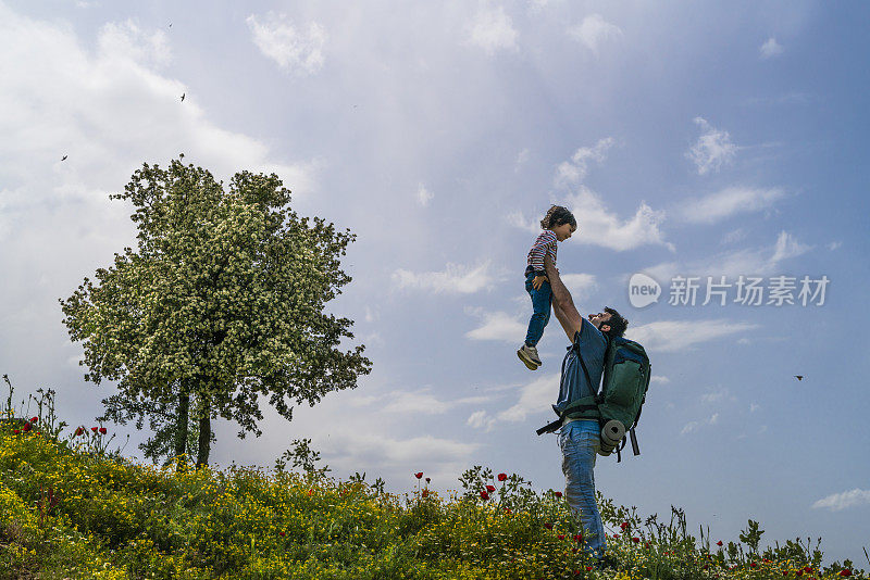 父亲在春天盛开的野花和山楂树的景观中将儿子举到空中。