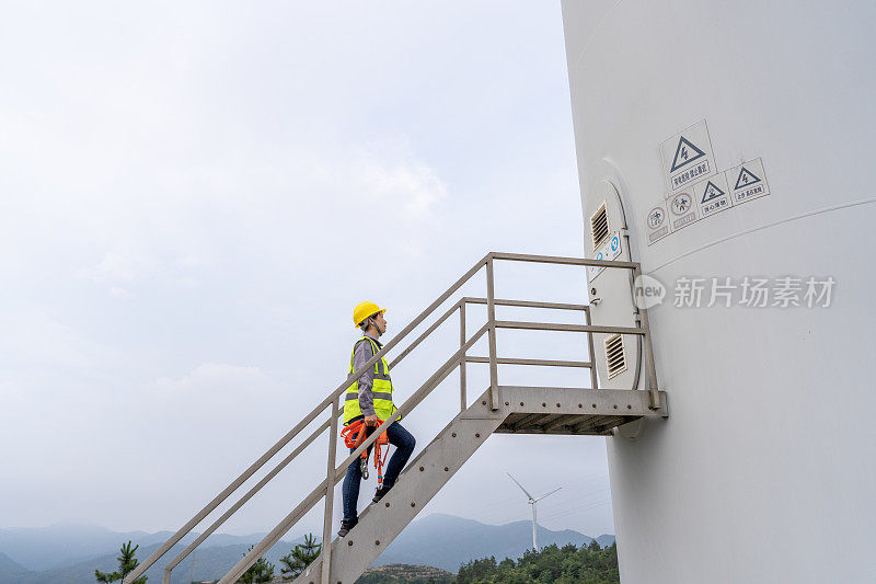 一名亚洲女工人正在爬风力涡轮机的梯子