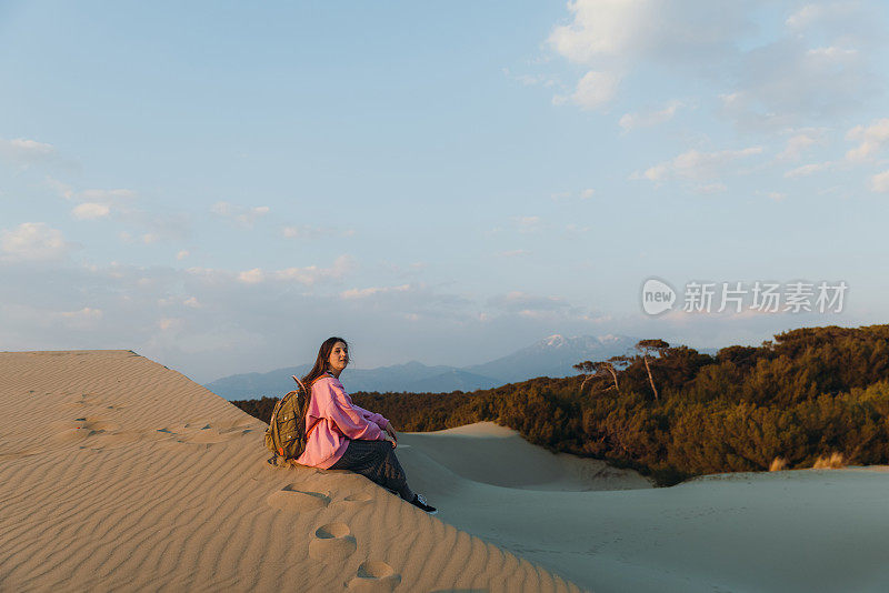 在土耳其海边的沙丘上，背着背包的女人凝视着风景优美的日落