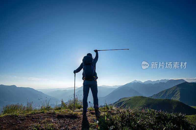 日落时分，山顶上的徒步者举着登山杆举起手臂