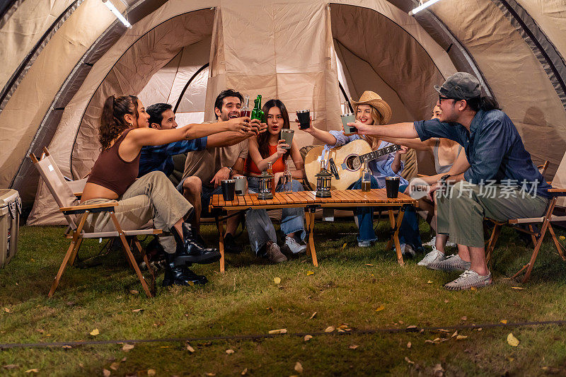 一群不同的朋友一起在帐篷里进行户外露营派对。迷人的年轻男女旅行者在音乐中跳舞，在自然森林度假旅行期间享受闲逛。
