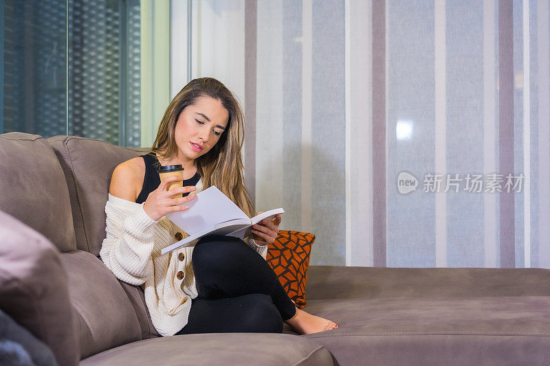 一个西班牙女人坐在沙发上，一边看书一边喝咖啡